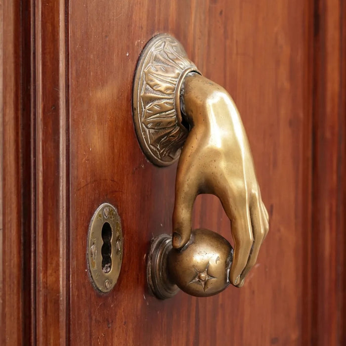 Brass door knocker in shape of human hand on varnished wood door 