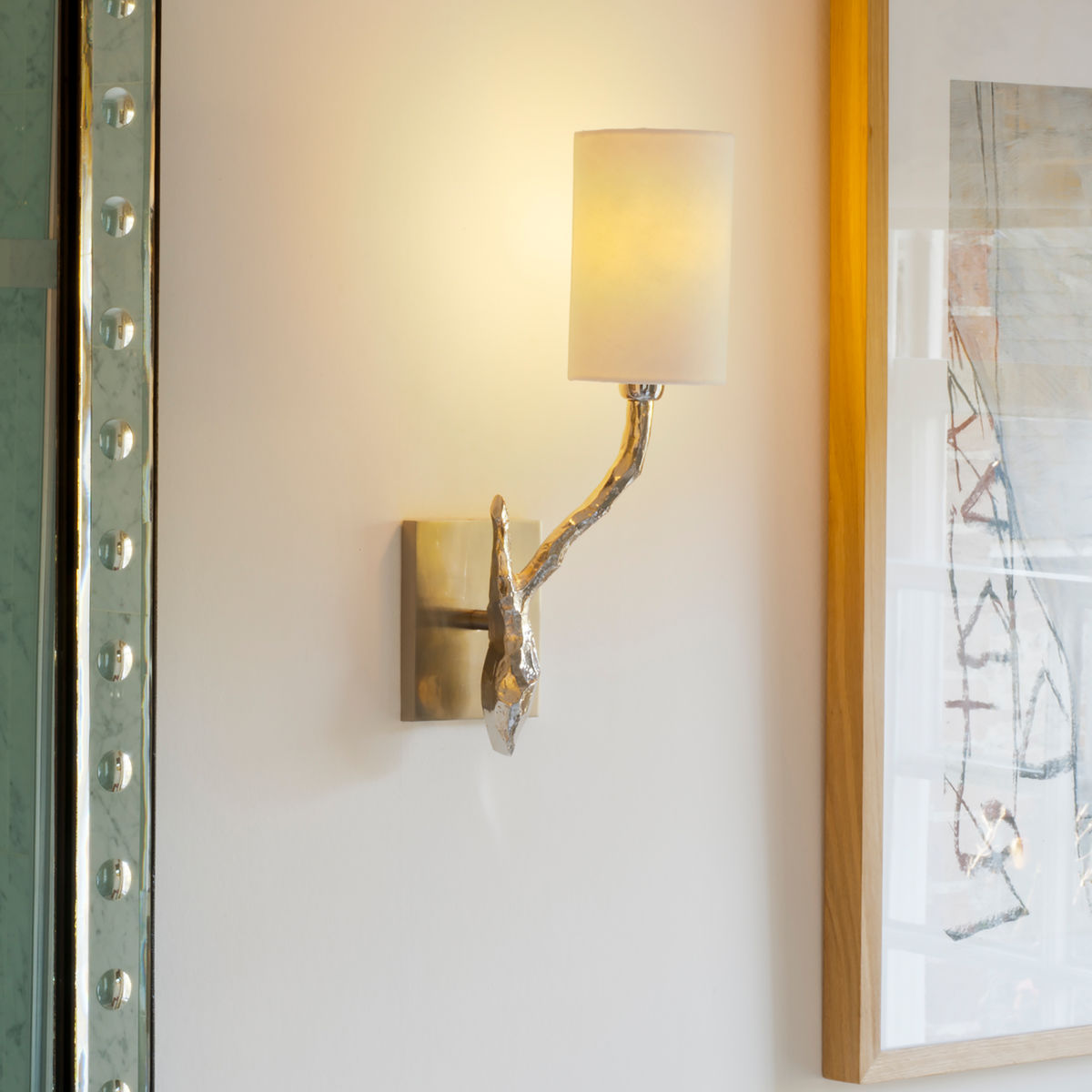 Plain cream cylindrical lampshade on brass wall light next to painting