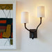 Half cylindrical lampshades on bronze wall light beside modern picture