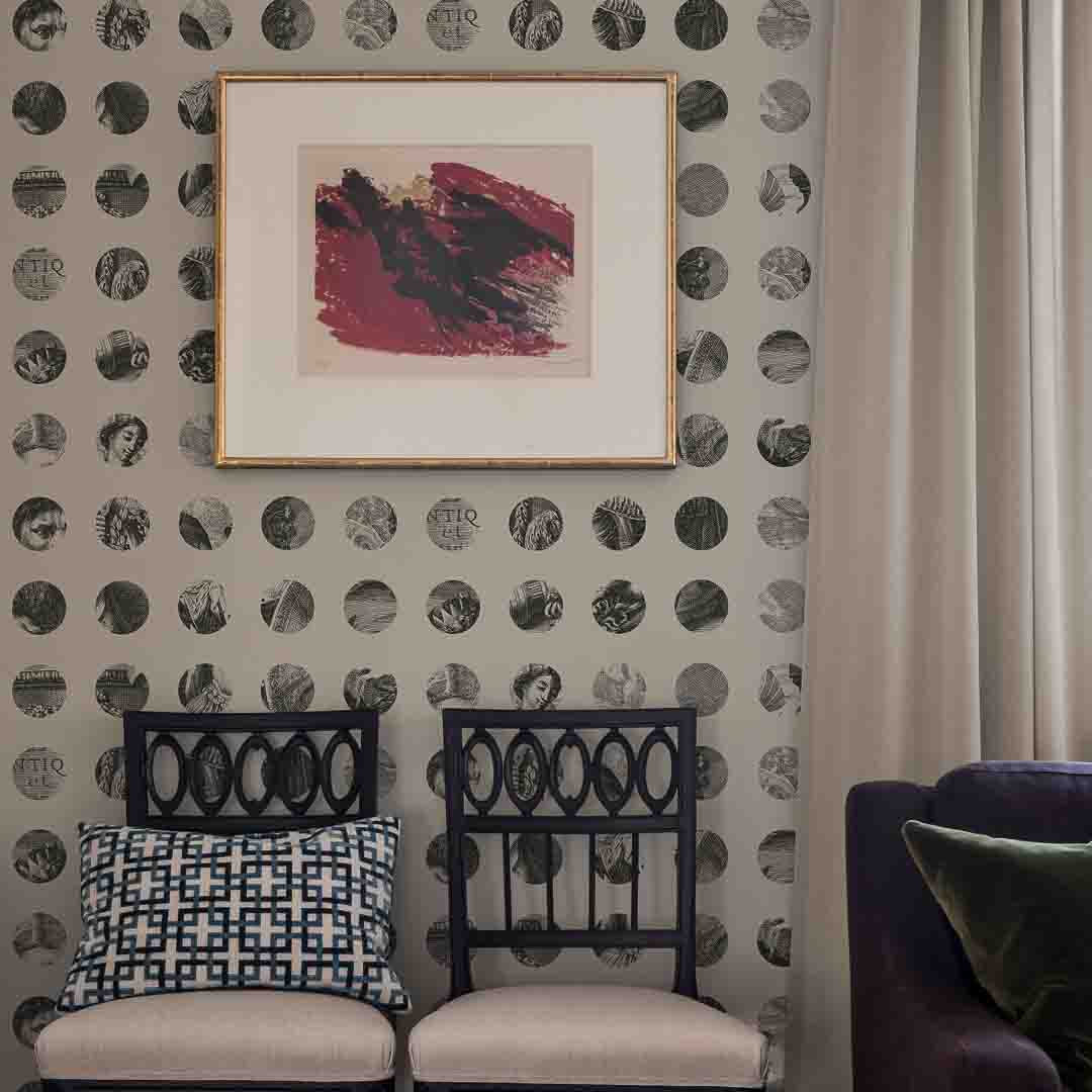 Decorative wall with circular pattern, framed artwork, and two chairs.