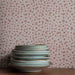 Stack of ceramic plates against a floral wallpapered wall