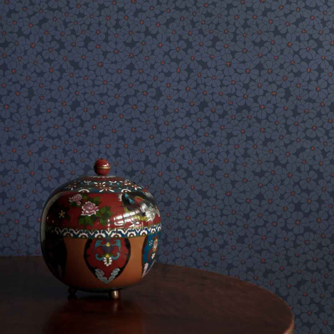 Decorative urn with floral patterns on a dark surface against a floral-patterned wall.