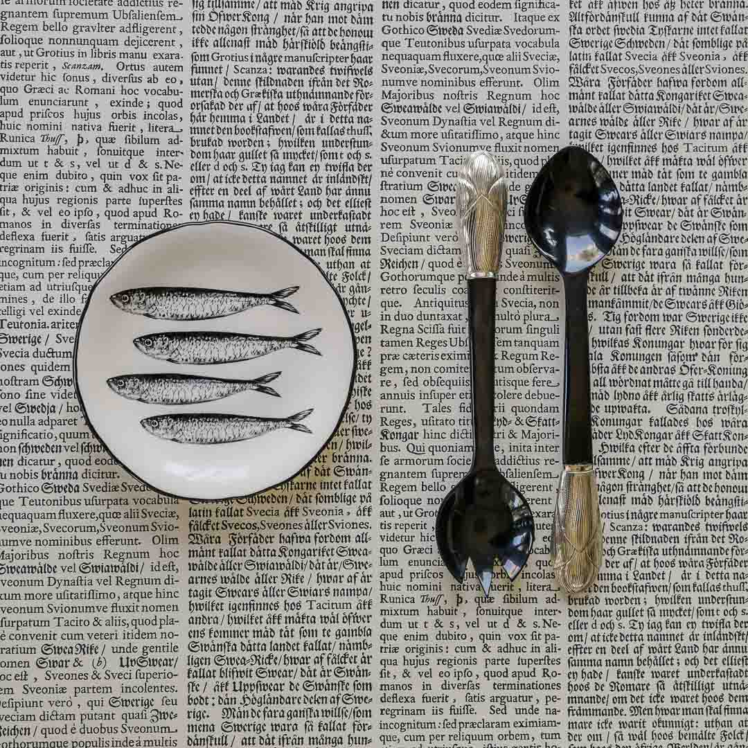 Decorative plate with fish design and two spoons on an old text background