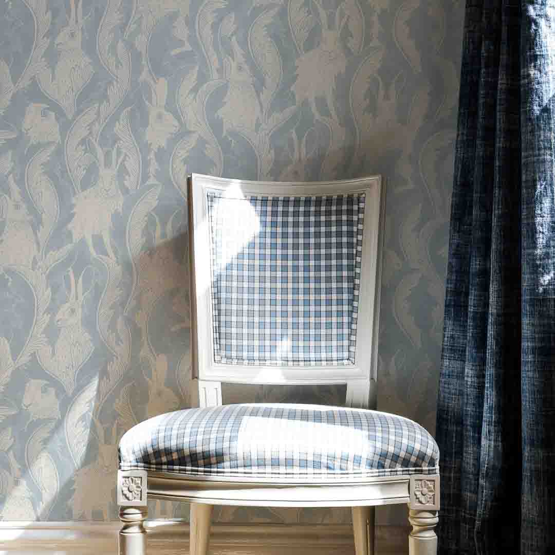 Chair beside blue curtain in front of washed denim blue wallpaper
