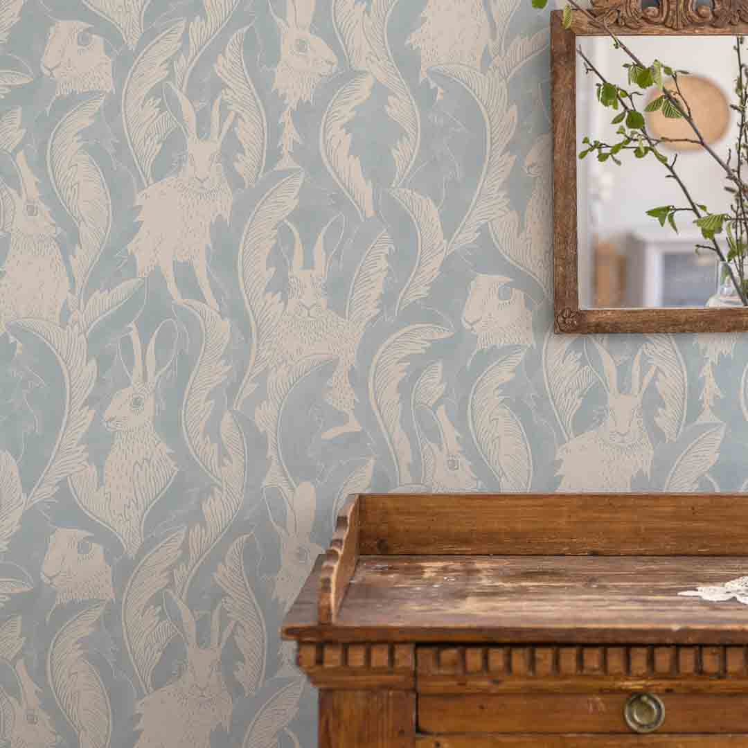 Wallpaper with rabbit and leaf pattern, wooden dresser below, mirror on wall.