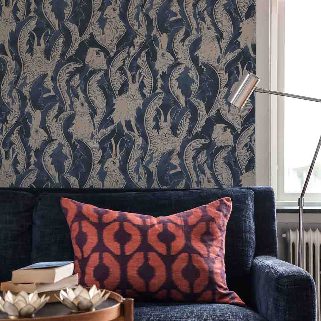 Patterned wallpaper with animal design above a blue sofa with a red and brown patterned pillow.