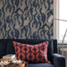 Patterned wallpaper with animal design above a blue sofa with a red and brown patterned pillow.