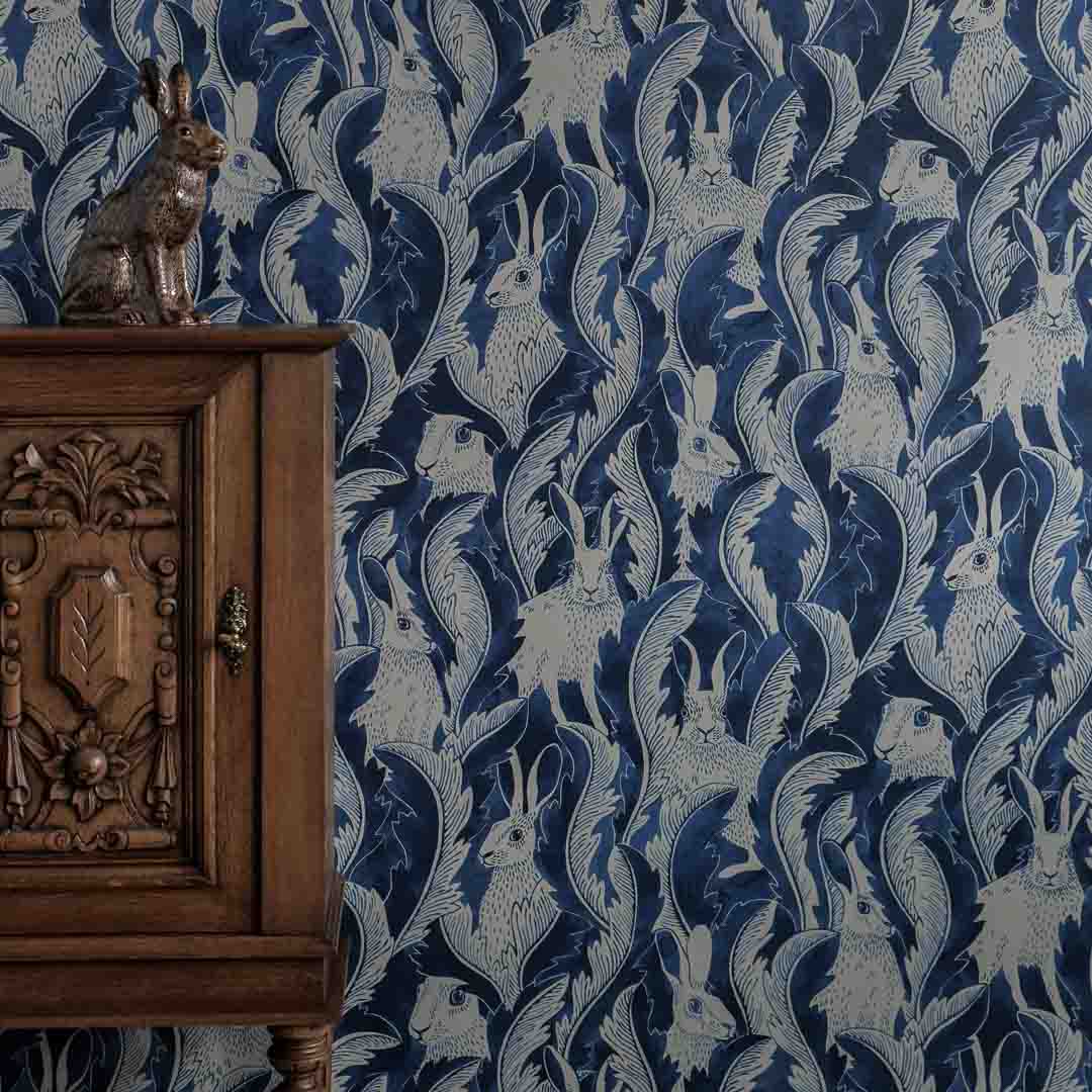 Wooden cabinet with intricate carvings against a blue wallpaper with hares pattern