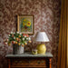 Decorative room interior with floral arrangement, lamp, and painting on patterned wall.