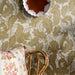 Wallpaper with animal and leaf pattern, floral pillow, and wicker chair.