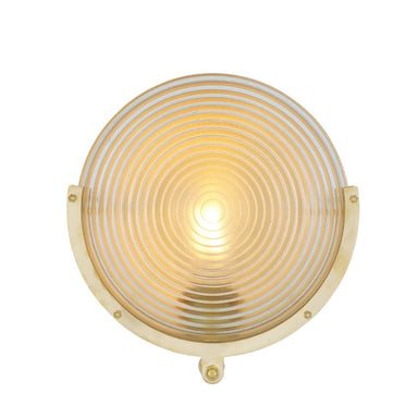 A round wall-mounted light fixture with a gold-toned metal frame and a ribbed glass shade that glows warm yellow when illuminated, shown against a plain white background.