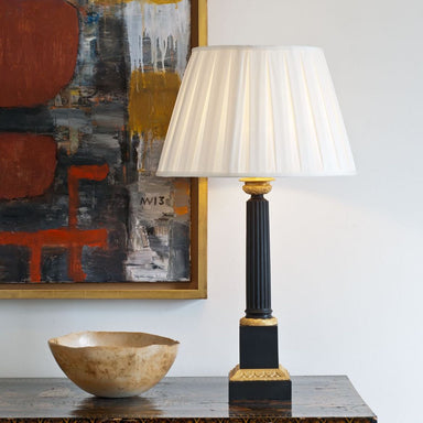 Bronze and gilt column lamp with cream silk shade on table with abstract picture