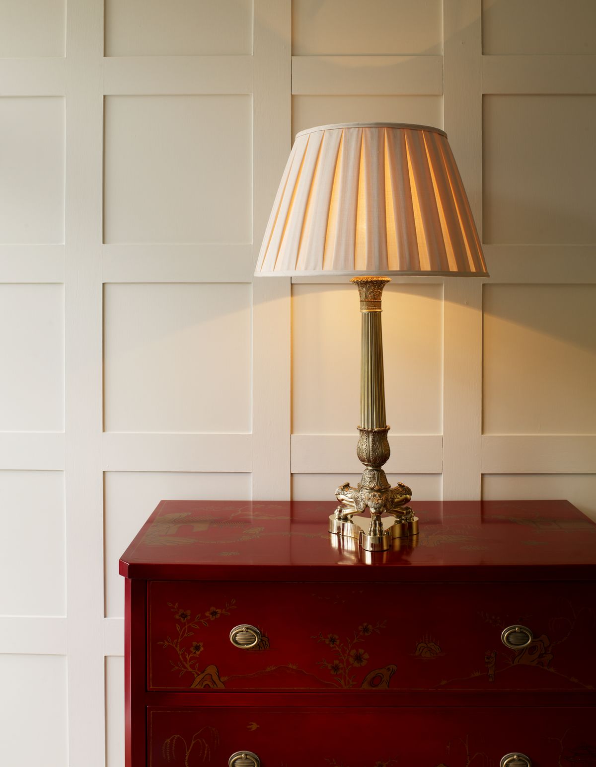 Brass column table lamp with silk pleated cream shade on mahogany chest