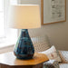 Cream card lampshade on modern green table lamp beside chair and painting