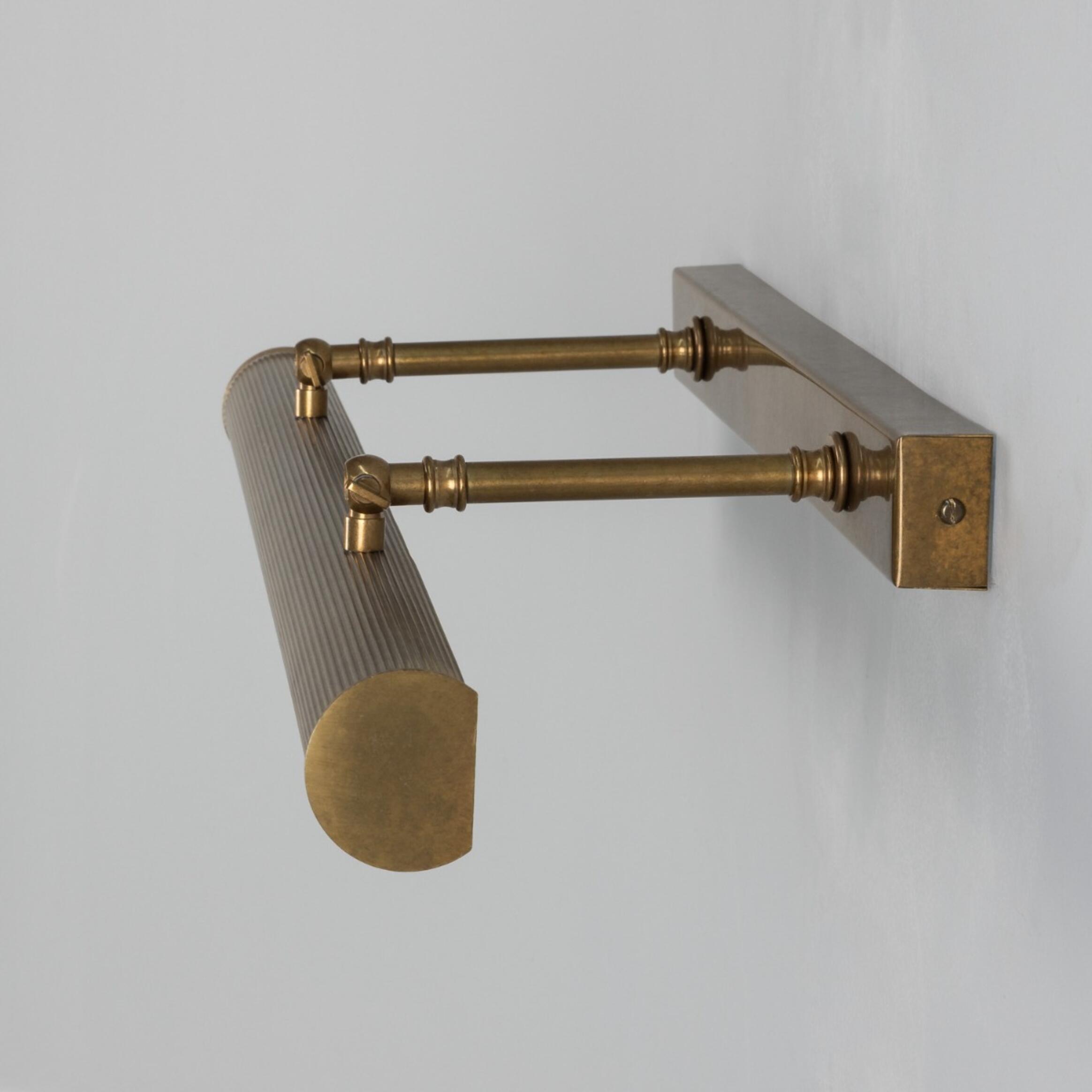 Brass wall-mounted lamp with cylindrical shade on a light gray background